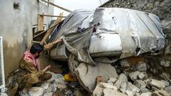 A villager inspects a damaged car among the debris of houses after a flash flood hit Charikar