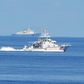 A Philippine coastguard ship BRP Langgam sails past a Chinese coastguard ship (background) near the Scarborough shoal in 2019