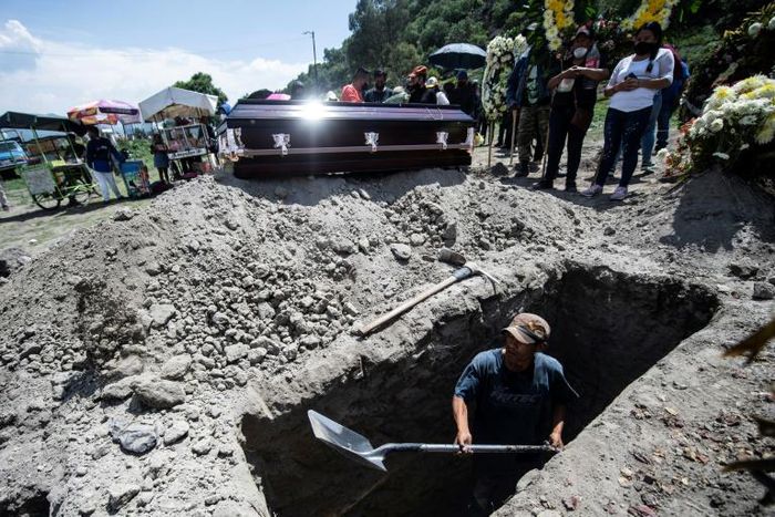 A grave is dug while a family waits during a funeral for a COVID-19 victim at the San Miguel Xico cemetery in Mexico