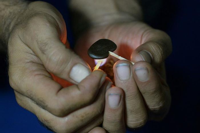 A Pakistani smoker holding a match to a clump of hashish to soften it before mixing it with cigarette tobacco