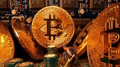 A small toy figure and representations of the virtual currency Bitcoin stand on a motherboard in this picture illustration