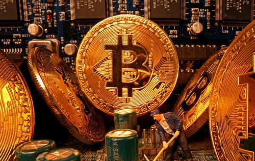 A small toy figure and representations of the virtual currency Bitcoin stand on a motherboard in this picture illustration