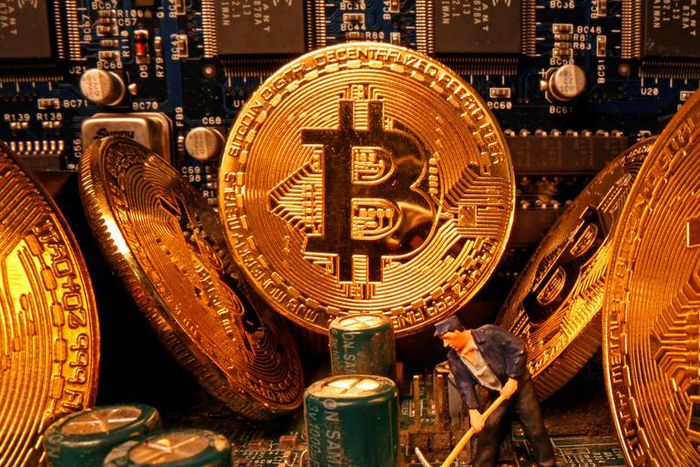 A small toy figure and representations of the virtual currency Bitcoin stand on a motherboard in this picture illustration