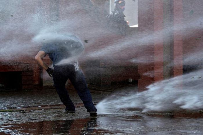 A demonstrator is hit by a jet from a water cannon during a protest in homage to the victims of Chile's 1973 military coup, in Santiago, September 2020
