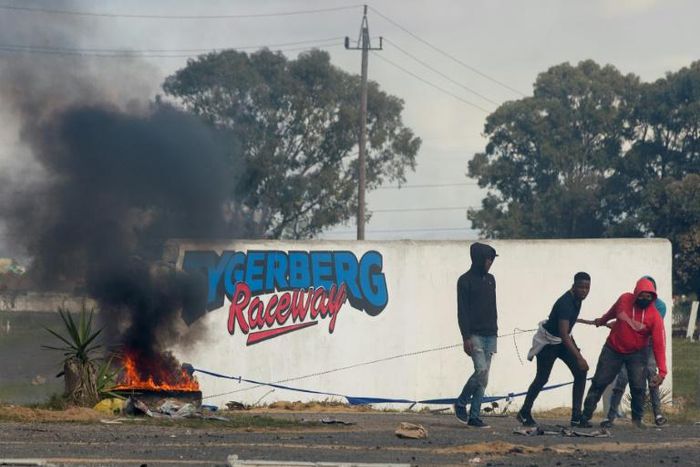 Young men haul a burning tyre during protests at Tygerberg Raceway near Cape Town. The motor-racing venue was invaded on August 6 by people demanding land