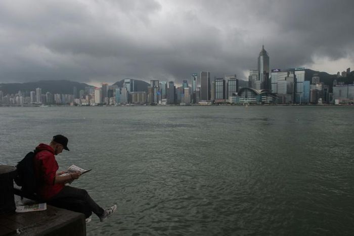 A man reads a newspaper on the edge of a promenade overlooking Victoria Harbour in Hong Kong
