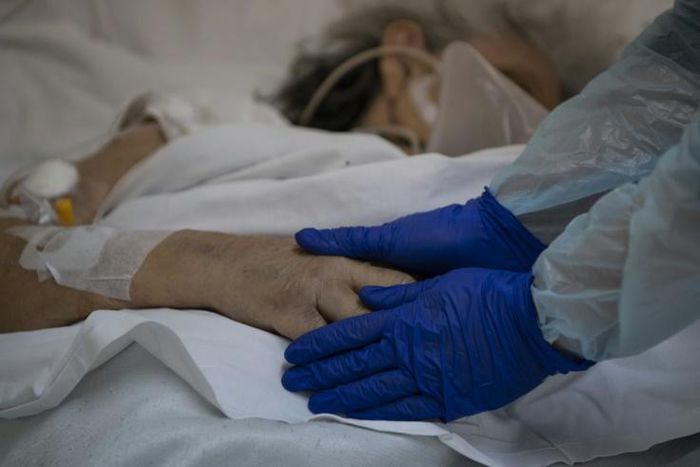 Dr Moyra Lopez holds the hand of a terminally ill patient at the Barros Luco hospital ward in Santiago where loved ones are able to see dying patients even if they have contracted the coronavirus