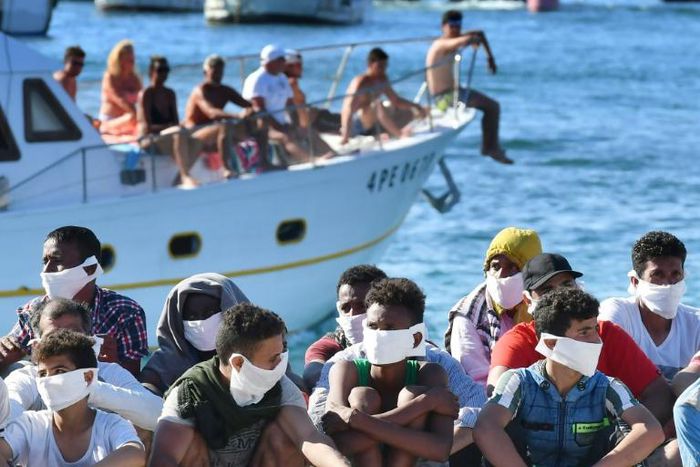 Many migrants land on the holiday destination of Lampedusa island, as sunbathers paddling in crystal waters look on