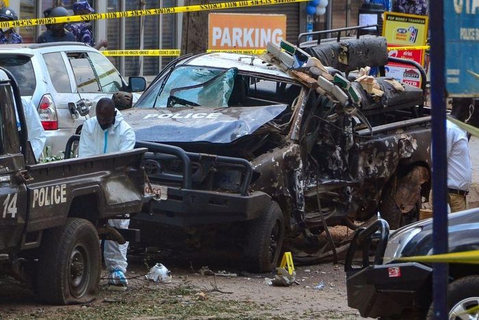 Police officers in Personal Protective Equipment (PPE) investigate around the police cars destroyed by a bomb explosion in front of Central Police Station in Kampala, Uganda, on November 16, 2021. - Two explosions hit Uganda's capital Kampala on Novemb...