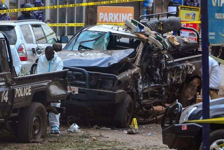 Police officers in Personal Protective Equipment (PPE) investigate around the police cars destroyed by a bomb explosion in front of Central Police Station in Kampala, Uganda, on November 16, 2021. - Two explosions hit Uganda's capital Kampala on Novemb...