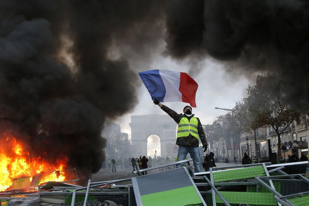 A demonstrator waves the French flag on a burning barricade on Paris’s Champs-Élysées avenue during a demonstration against the raising of fuel taxes on Novermber 24, 2018. Michel Euler/AP