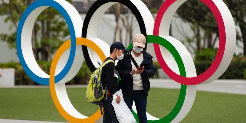 People in Japan wear masks due to the COVID-19 pandemic in front of Olympics rings.