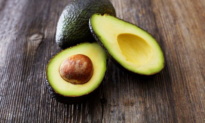 Whole and sliced avocado on wood