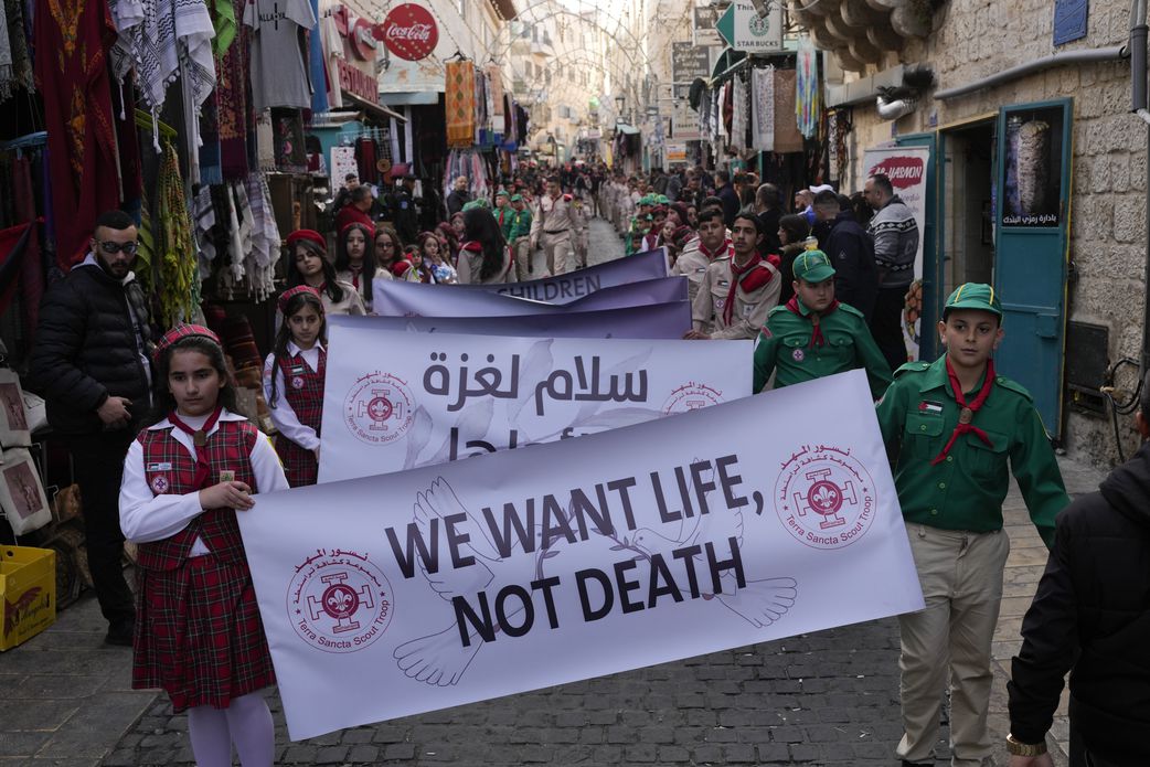 Scouts hold a sign that reads "We want life, not death" during the traditional Christian procession towards the Church of the Nativity, traditionally believed to be the birthplace of Jesus, on Christmas Eve. [Matias Delacroix/AP Photo]