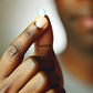 A close-up image of a Black man's hand holding a small, white pill between his thumb and forefinger, poised to take the medicine The background is so