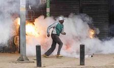 A protester flees with a teargas cannister exploding in the background during protests in Nairobi