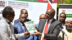 Immigration and Citizen Services PS Julius Bitok presents a copy of the Braille version of  a booklet on Frequently Asked Questions (FAQs) on Digital ID to Daniel Njuguna of the National Council of Persons with Disability at the Nairobi Serena Hotel
