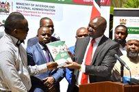 Immigration and Citizen Services PS Julius Bitok presents a copy of the Braille version of  a booklet on Frequently Asked Questions (FAQs) on Digital ID to Daniel Njuguna of the National Council of Persons with Disability at the Nairobi Serena Hotel