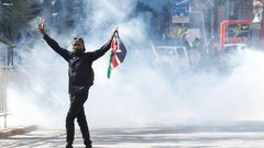 A protester carries a flag of Kenya amid teargas fired by riot police during protests