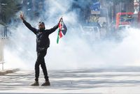 A protester carries a flag of Kenya amid teargas fired by riot police during protests