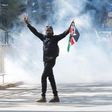 A protester carries a flag of Kenya amid teargas fired by riot police during protests