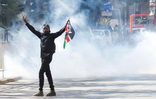 A protester carries a flag of Kenya amid teargas fired by riot police during protests