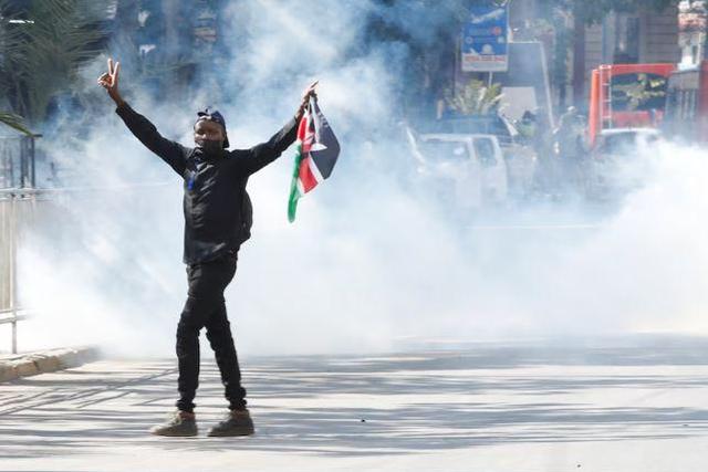 A protester carries a flag of Kenya amid teargas fired by riot police during protests