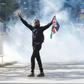 A protester carries a flag of Kenya amid teargas fired by riot police during protests