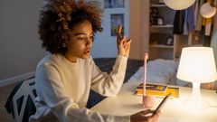 A teenager sitting on a desk while holding a phone [Image Credit: Cottonbro Studio]