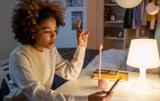 A teenager sitting on a desk while holding a phone [Image Credit: Cottonbro Studio]