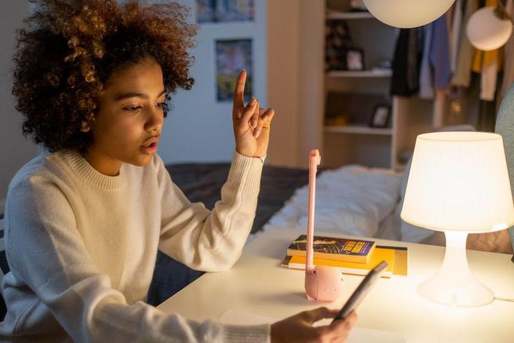 A teenager sitting on a desk while holding a phone [Image Credit: Cottonbro Studio]