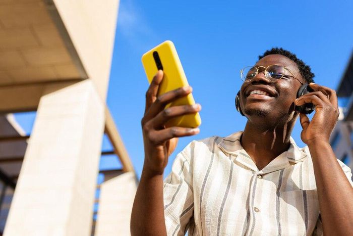 A young man relaxing outdoors listening to music using phone and headphones