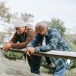 Black father conversing with teenager near fence on farmland [Image: Any Lane]