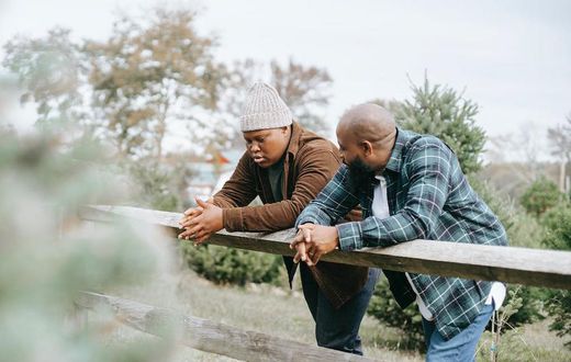 Black father conversing with teenager near fence on farmland [Image: Any Lane]