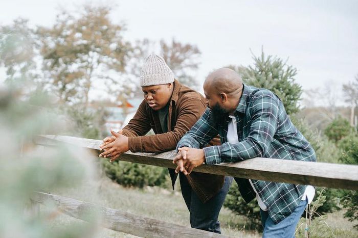 Black father conversing with teenager near fence on farmland [Image: Any Lane]