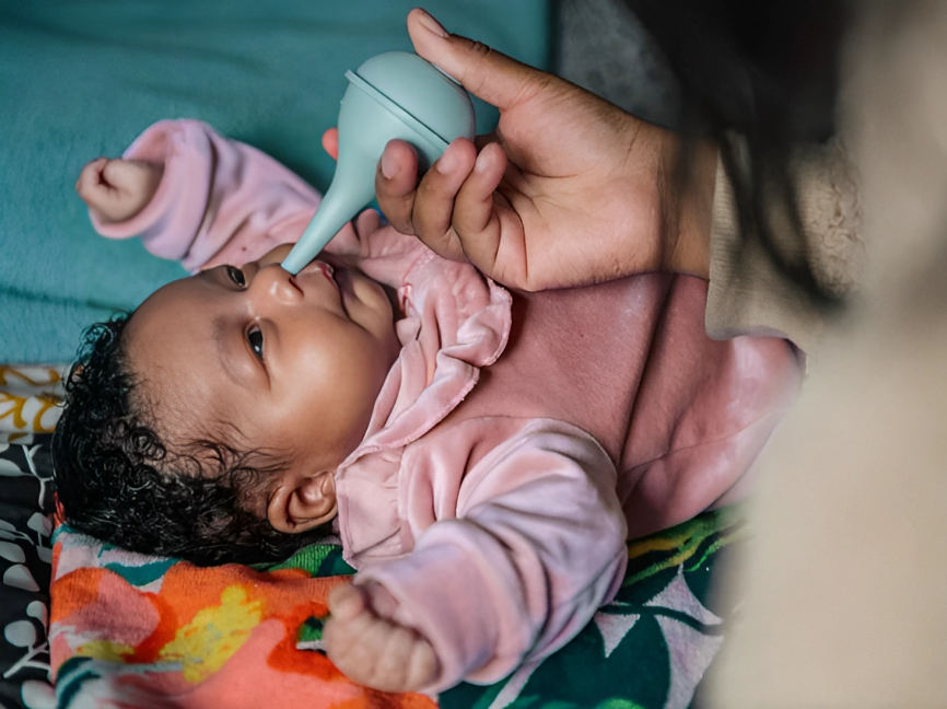 A parent sucking out mucus from a new born's nose  using an aspirator