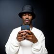 Portrait of handsome young man wearing white sweatshirt and black bucket hat, using mobile phone. Studio shot on black background.