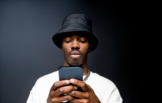 Portrait of handsome young man wearing white sweatshirt and black bucket hat, using mobile phone. Studio shot on black background.