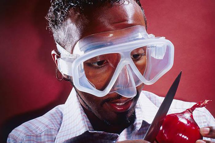 A stock photo of a man wearing a mask to cut an onion