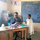 Photo showing the teacher mending school uniform for a girl in Narok county