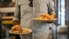 Man in plaid shirt holding two plates with crisps and sandwiches [Credit: Rachel Claire]