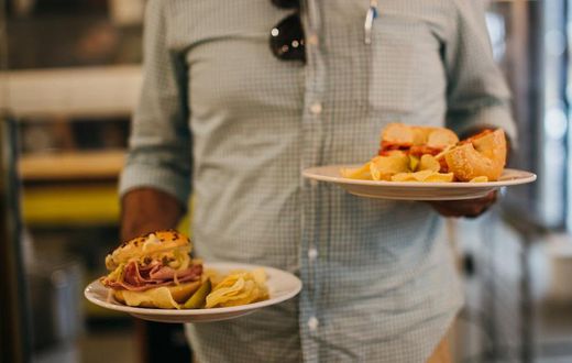 Man in plaid shirt holding two plates with crisps and sandwiches [Credit: Rachel Claire]