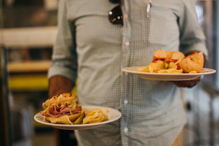 Man in plaid shirt holding two plates with crisps and sandwiches [Credit: Rachel Claire]