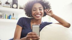 Smiling African American woman texting with cell phone on living room sofa