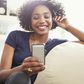 Smiling African American woman texting with cell phone on living room sofa