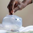 A person putting a coin into a savings piggy bank [Image credit: Joslyn Pickens]