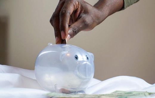 A person putting a coin into a savings piggy bank [Image credit: Joslyn Pickens]
