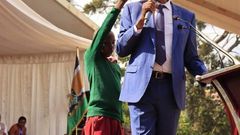 Young learner holding an umbrella for CS Machogu during a public function in Murang'a