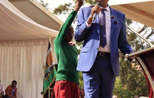 Young learner holding an umbrella for CS Machogu during a public function in Murang'a