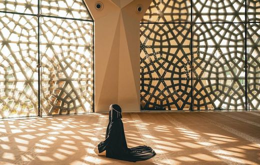 Woman praying in a mosque with openwork windows {image Credit: Hatice Baran]